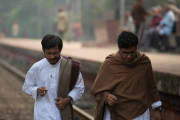 Young Indian Bengali detective and his colleague with traditional wear walking on a railway track and having a discussion in a winter morning. Indian lifestyle.