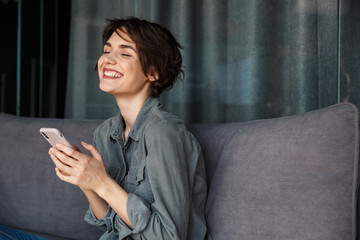 Image of beautiful young joyful woman using mobile phone and laughing