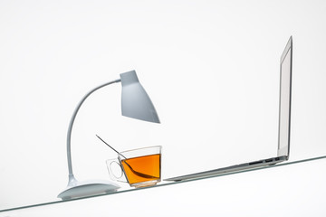 table lamp with tea cup and laptop on inclined glass table surface 