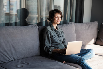 Image of nice young pleased woman using laptop and smiling