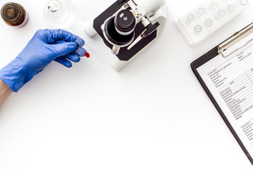 Clinical science research with microscope. Hand holds blood sample on white background top view copy space
