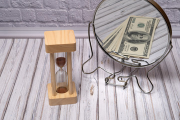 Hourglass on the table. Money is reflected in the mirror