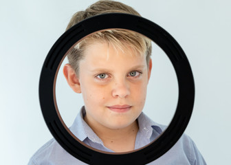 young blond boy is looking through the black ring. 