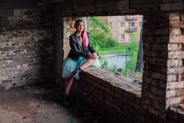 Fototapeta na wymiar Portrait of a young girl with pink hair sitting on the windowsill inside of collapsed building surrounded by ruins
