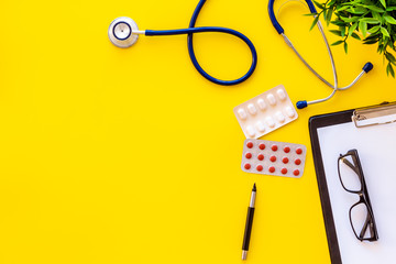 Doctor office desk with medicine. Yellow background top view copy space