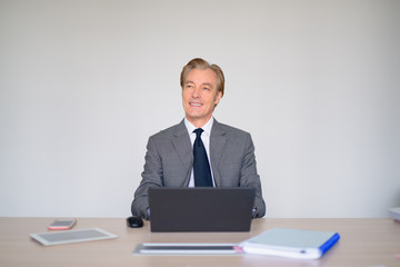 Happy mature handsome businessman thinking while using laptop at work