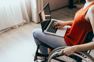 Woman in a wheelchair at home with a laptop on her lap, hand close up, unrecognizable man.
