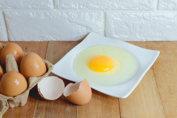 Eggs in paper trays and hammered eggs are on a white plate with an egg shell on the side, placed on a wooden table in the kitchen with a brick background.