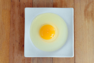 Eggs hammered on a white plate placed on a wooden table in the kitchen.top view