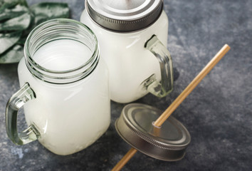 Coconut water tropical drink in glass jar with handle on dark background with copy space