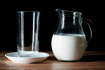 Una taza de cristal vacía y una jarra de leche de vaca en una mesa de madera