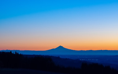 A sunrise scene in Oregon, with the iconic peak of Mt. Hood on the horizon in silhouette, vivid color behind.