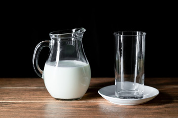 Una taza de cristal vacía y una jarra de leche de vaca en una mesa de madera