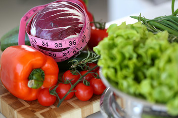 Measuring tape lying on a table with fresh vegetables closeup. Concept slimming recipes aganist kitchen background.