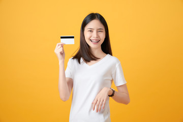 Attractive smiling Asian woman holding credit card payment on yellow background with copy space.