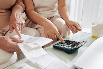 Close-up image of senior woman and her adult daughter calculating sum of unpaid bills