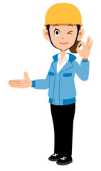 右側を紹介しOKのサインを示すヘルメットを着用し青い作業着を着た女性
