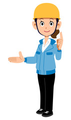 右側を紹介し人差し指を建てるヘルメットを着用し青い作業着を着た女性
