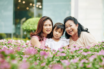 Portrait of three generation of Vietnamese family sitting among blooming flowers and looking at camera