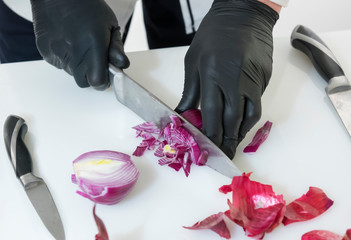 Chef cook cut red onion with a knife at the white table