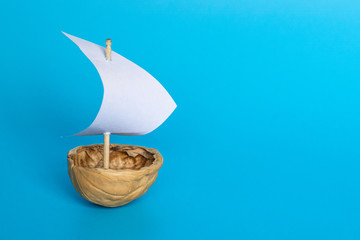 Fototapeta premium a small boat made of nutshell with a white sail on the blue background. Journey banner template.