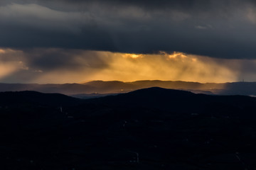 Obraz premium Sunrays coming over mountains beneath moody clouds