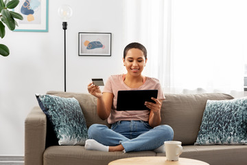 Fototapeta premium internet banking, online shopping and technology concept - happy smiling african american woman sitting on sofa with tablet pc computer and credit card at home