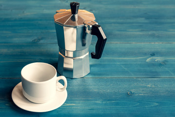 Cup and saucer for coffee and a geyser coffee maker on a blue wooden table