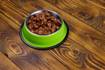 Canned food for cats or dogs in green metal bowl on wooden floor