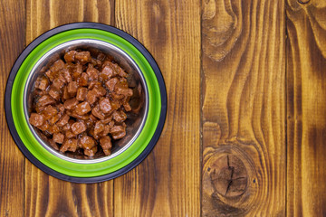 Canned food for cats or dogs in green metal bowl on wooden floor. Top view