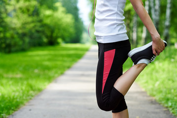 young fitness woman runner stretching legs before run on grass