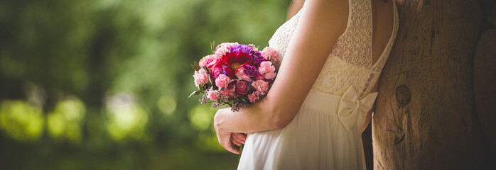 A woman in a cream dress holds a beautiful wedding bouquet of flowers on a background of green park. Bride.