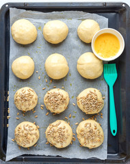 Pieces of raw dough on a pan, silicone brush, egg, seeds. Cooking homemade buns. Top view
