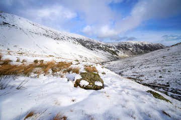 Fototapeta na wymiar A snow covered Glenridding Beck below Catstye Cam with Glenridding Screes in the distance on a sunny winters day in the Lake District, UK.