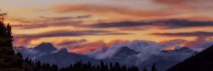 Wide angle panorama silhouette forest and mountain tops in red orange blue clouds gradient sunset