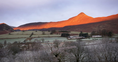 A frost covered valley of Newlands with a winters sunrise catching the mountain top of Causey Pike, Derwent Fells in the Lake District.