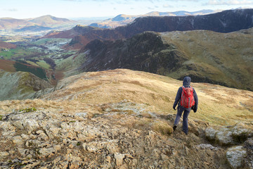 A hiker descending the rocky mountain ridge from the summit of Robinson towards High Snab Bank on a cold winters day in the Lake District, UK.