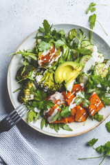 Baked sweet potato, broccoli and avocado salad bowl with tahini dressing, top view. Vegan food concept.