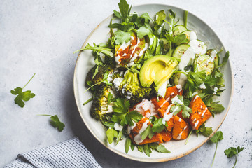 Baked sweet potato, broccoli and avocado salad bowl with tahini dressing, top view. Vegan food concept.