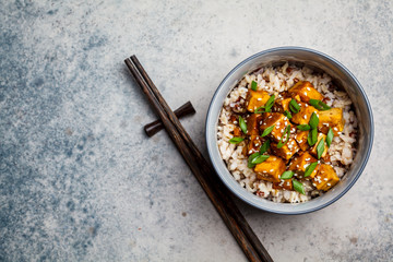 Marinated tofu with sesame seeds, green onions and brown rice, top view. Asian food concept.