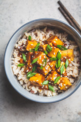 Marinated tofu with sesame seeds, green onions and brown rice, top view. Asian food concept.