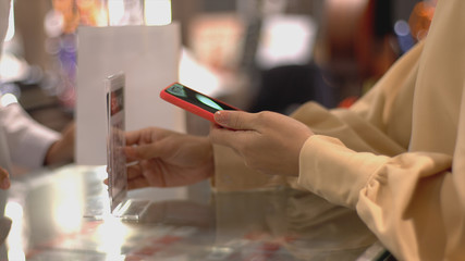 An upwardly mobile Asian Muslim woman using a mobile phone - smartwatch to pay for a product at a sale terminal with nfc identification payment for verification and authentication