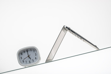 white clock and laptop in a bright office on a glass table