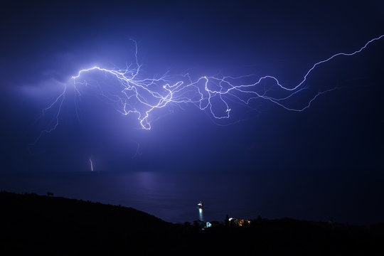 Huge lightning in the sky over the sea and the coast with a small village