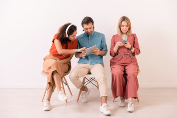 Brown-haired man sharing information on internet with Afro-American woman in wireless headphones while blonde girl texting sms