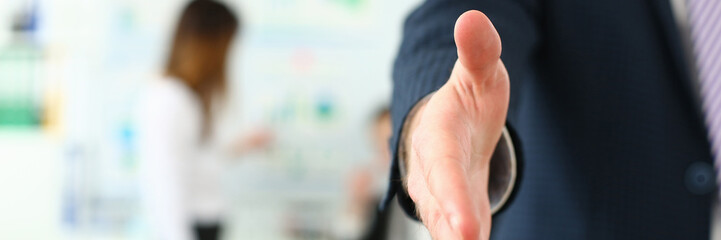 Focus on man stretching out to shake hands with colleague or boss. Younger managers working on new business strategy for corporate people. Company meeting concept. Blurred background