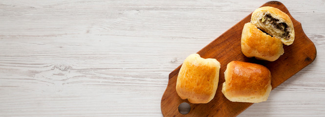 Home-baked Beef Russian Bierocks on a rustic wooden board on a white wooden surface, top view. Flat lay, overhead, from above. Space for text. © Liudmyla