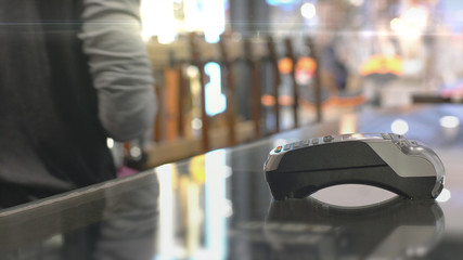 An upwardly mobile Asian Muslim man using a mobile phone - smartwatch to pay for a product at a sale terminal with nfc identification payment for verification and authentication