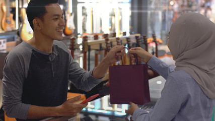 An upwardly mobile Asian Muslim man using a mobile phone - smartwatch to pay for a product at a sale terminal with nfc identification payment for verification and authentication