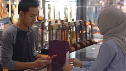 An upwardly mobile Asian Muslim man using a mobile phone - smartwatch to pay for a product at a sale terminal with nfc identification payment for verification and authentication